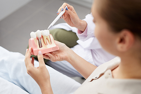 A person holding a tooth model while sitting in a dental office chair.